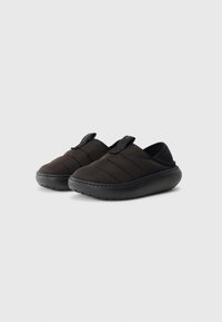 Svarta kviltade slip-on skor med rund tå, texturerad gummisula och elastisk remdetalj. Materialet verkar mjukt och hållbart.