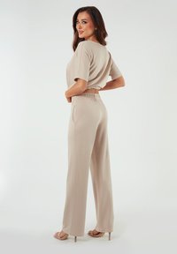 Beżowy, krótkotrwały top z krótkim rękawem w połączeniu z spodniami o wysokim stanie i szerokich nogawkach. Miękka tkanina, elastyczny pas i kieszenie boczne.