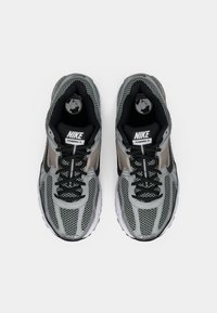 Ténis Nike Vomero 5 em cinza com detalhes em preto, apresentando uma parte superior em malha, sola acolchoada e atacadores pretos. Projetados para conforto e suporte.