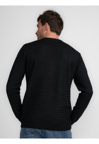 Maglione nero a coste con colletto rotondo e motivo testurizzato, maniche lunghe e vestibilità comoda. Presenta una finitura liscia e orlo con risvolto.