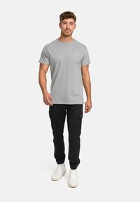 Graues T-Shirt mit kurzen Ärmeln, lässiger Schnitt, mit Rundhalsausschnitt. Kombiniert mit schwarzen Cargo-Hosen mit Seitentaschen und elastischen Bündchen. Weiße Sneakers.