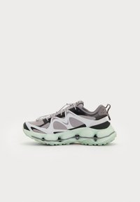 Baskets Nike présentant une tige en mesh grise et blanche avec une semelle rembourrée verte et des accents noirs. Forme dynamique avec un design distinctif.