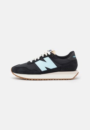 Zwart en lichtblauwe New Balance lage sneaker met witte veters en een gumkleurige zool op een effen lichte achtergrond.