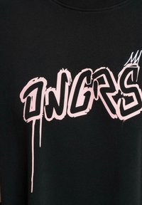 Čierna mikina s veľkým ružovým graffiti štýlom písma, ktoré hovorí "ONGRS", so kvapkami, ktoré sa tiahnu od textu.