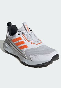 Grijze sportieve schoen met een bovenwerk van mesh en oranje accenten, een gestructureerde tussenzool en een robuuste zwarte buitenzool voor grip.