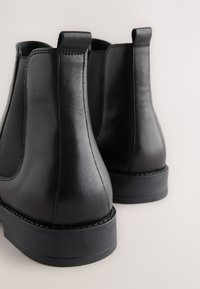 Čierne kožené Chelsea topánky s elastickými bočnými panelmi, zaokrúhlenou špičkou a odolnou gumovou podrážkou. Majú pútka na ľahké obúvanie.