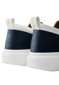 Sneaker navy e bianca con tomaia in pelle liscia, con linguetta sul tallone a contrasto e suola bianca spessa. Presenta il nome del marchio in rilievo sulla suola.