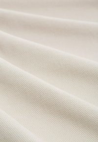 Un tissu couleur crème avec une texture fine et densément tissée, présenté en plis diagonaux doux créant une apparence lisse et fluide.