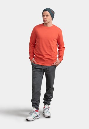 Oranje sweatshirt, donkergrijze joggers en witte sneakers met multicolore accenten; gebreide grijze beanie; relaxte pasvorm, casual stijl.