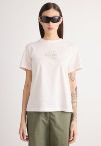 Ροζ βαμβακερό μπλουζάκι με κοντά μανίκια και στρογγυλή λαιμόκοψη. Διαθέτει έντονο μπεζ λογότυπο Calvin Klein στο στήθος.