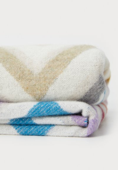 Wool blanket in a folded stack, featuring a cream base with geometric patterns in blue, purple, beige, and gray. Soft texture.