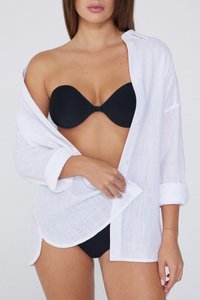 Chemise en lin blanche, déboutonnée, avec des manches retroussées. Soutien-gorge noir sans bretelles visible en dessous. Texture de tissu lisse, coupe décontractée.