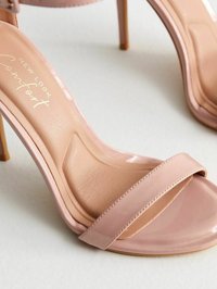 Sandalias de tacón alto y abierta en la parte delantera, fabricadas en material sintético brillante de color rosa claro. Presentan una amplia correa frontal y una plantilla texturizada con texto en relieve.