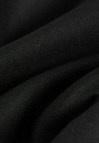 Musta kudottu kangas, jolla on teksturoitu pinta, esittäen pehmeitä taitoksia ja tasaista väriä. Kankaalla on sileä, kestävä tuntuma.