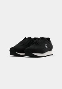 Black athletic shoes with a textured fabric upper, lace-up design, and a white rubber sole. Features logo on outer side.