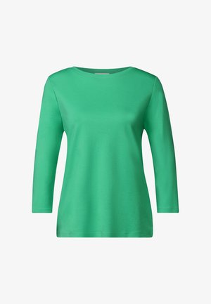 Pitkähihaisessa vihreässä T-paidassa on pehmeää puuvillakangasta, pyöreä kaula-aukko ja normaali istuvuus. Se on sileä ja siinä ei ole näkyviä kuvioita tai yksityiskohtia.