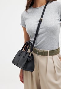 Melna ādas rokas soma ar divām rokturiem un noņemamu siksniņu. Funkcijas ietver priekšējo kabatu, gludu tekstūru un smalkus izšuvumu elementus.