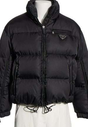 Doudoune noire Prada avec col montant, fermeture éclair devant, poche poitrine zippée et cordon de serrage à l'ourlet sur un buste de mannequin blanc.