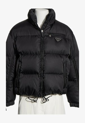 Doudoune noire Prada avec col montant, fermeture éclair devant, poche poitrine zippée et cordon de serrage à l'ourlet sur un buste de mannequin blanc.
