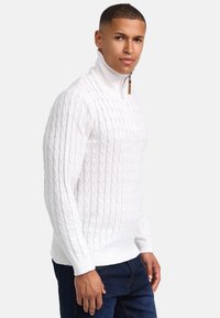 Weißer Kabelstrickpullover mit hohem Kragen und halbem Reißverschluss, ausgestattet mit gerippten Bündchen und Saum. Glatte Textur mit einem klaren, sauberen Design.