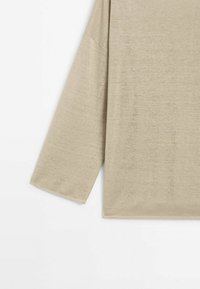 Chemise beige à manches longues avec une coupe ample, montrant la manche gauche et une partie du torse sur fond blanc.