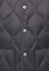 Grå quiltet vest med diamantmønster, sølvfargede trykknapper og teksturert kant. Har en sidelomme. Mykt, luftig materiale.