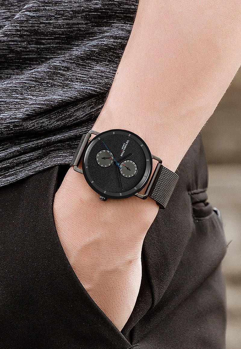 Orologio analogico nero con due sottodial su un quadrante nero testurizzato. Presenta un cinturino in rete metallica e una cassa rotonda minimalista.