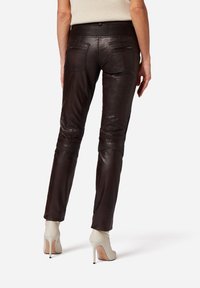 Bruine leren broek met een slim-fit ontwerp, voorzien van gestikte details en een ritssluiting op de achterzakken, gecombineerd met witte hoge hakken.