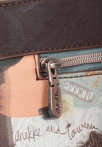 Texturiertes, braunes Kunstleder mit einem mehrfarbigen Design. Silberner Reißverschluss mit geprägtem "Anekke"-Schriftzug. Inklusive gemusterter Akzente und Nähte.