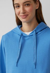 Felpa con cappuccio azzurro chiaro dal tessuto morbido, con stringhe etichettate "S.Oliver." Design semplice e vestibilità classica.