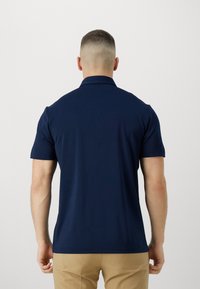 Marinblå polo t-shirt i slät, elastisk tyg. Kort ärm och krage med en ren, tight design. Bakvy visar enkelhet och passform.