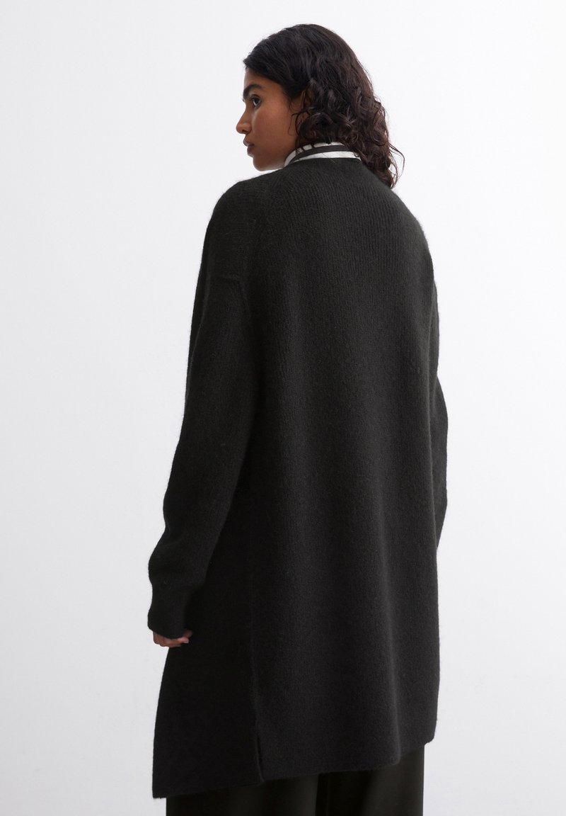 Langer schwarzer Strickcardigan mit strukturiertem Finish, überschnittenen Schultern und geradem Schnitt, der bis unter die Hüften reicht.