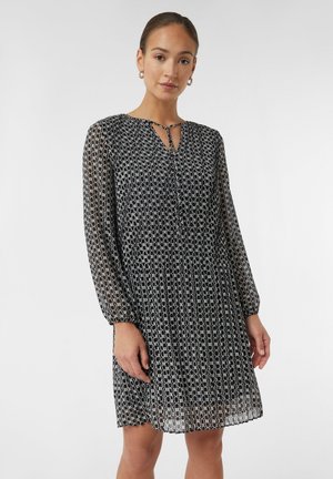 Robe à motif noir et blanc avec de longues manches transparentes, un décolleté en forme de clé et une silhouette fluide. Le matériau semble léger avec une finition texturée.