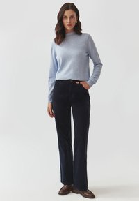 Světle modrý svetr s dlouhým rukávem a vysokým límcem, v kombinaci s námořnickými manšestrovými kalhotami. Celý outfit doplňují hnědé kotníkové boty.