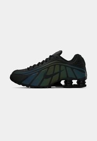 Sneaker Nike con tomaia nera, accenti degradè verdi e blu, texture in rete e un tallone distintivo con ammortizzazione simile a una molla.