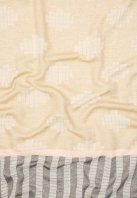 Tkanina w kolorze kremowym z teksturowanym wzorem w kształcie siatki na gładkiej powierzchni. Dolna część posiada wzór w szaro-białe paski.