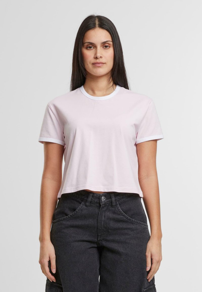 Lys rosa cropped t-skjorte med korte ermer og hvit ribbestrikket hals, laget av glatt stoff. Brukt med høyt liv svarte bukser.