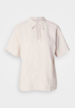 Blusa de linho em bege claro, com colarinho redondo e fecho com laço, mangas curtas e bainha reta com textura subtil.