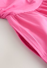 Lyserød kjole med en glat, skinnende tekstur. Har rynkede detaljer og en flydende silhuet. Synlige sømme langs kanten og siderne.