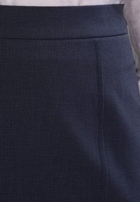 Marinhärdad blå tygkjol med subtila rutor, med en slät midja och skräddarsydd plissering fram.