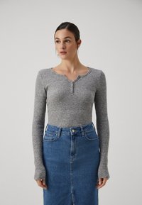 Lys grå ribbet langermet topp med rund hals og knappdetaljer, kombinert med et høy midje blå denimskjørt.