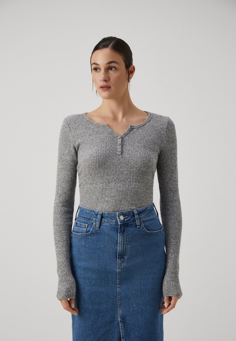 Lys grå ribbet langermet topp med rund hals og knappdetaljer, kombinert med et høy midje blå denimskjørt.