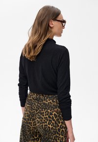 Kobieta o jasnobrązowych włosach, nosząca okulary w tortoishell, czarną, strukturalną bluzkę z długim rękawem i spódnicę w leoparda z wysokim stanem, odwrócona plecami.