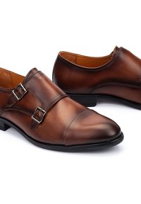 Bruine leren dresschoenen met twee zilveren gespen, puntige neus, gladde textuur en een zwarte rubberen zool. Klassiek ontwerp voor formele kleding.