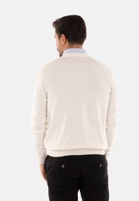 Maglione color crema con scollo rotondo, maniche lunghe e polsini a coste, abbinato a pantaloni neri con tasche posteriori dotate di bottoni.