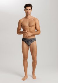 Slip da bagno aderenti da uomo in grigio scuro con un motivo floreale strutturato e una cintura solida, realizzati in un tessuto elastico e leggero.