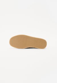 Semelle d'une chaussure en caoutchouc texturé avec de petits motifs circulaires, offrant adhérence et durabilité.