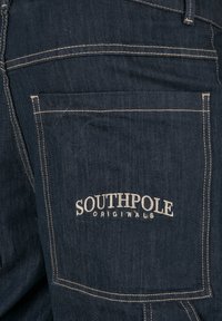 Dark denim jeans featuring a large back pocket with white stitched outline and "SOUTHPole" logo in white text above "ORIGINALS."