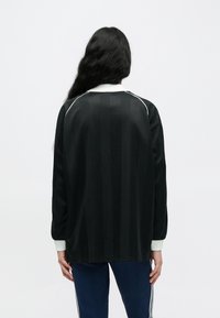 Čierny dlhý rukáv dres s vertikálnymi pruhmi, bielym golierom a kontrastnými detailmi na ramenách. Hladká textúra, voľný strih.