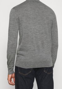 Ljust grå tröja med långa ärmar och rund halsringning. Mjuk textur, smal passform, minimala sömmar och en slät yta. Bärs med mörka jeans.